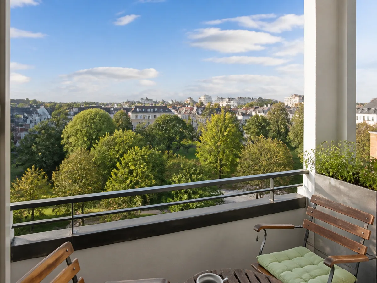 Balkon einer Stadtwohnung mit Blick auf Park, Dächer und weiten Himmel